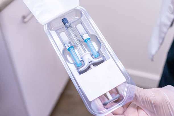 Doctor holding package of dermal filler with syringe vial and needles, for performing a softlift, or non-surgical facelift with MD Codes on a medical cosmetic patient. Contains hyaluronic acid (HA) for an anti-aging beauty treatment.