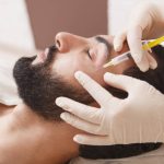 Bearded man getting anti-wrinkle face filler treatment by beautician