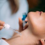 Neck anti-aging treatment. Cosmetician Applying Hyaluronic Acid Serum on Woman’s Neck