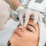 The doctor cosmetologist makes the Rejuvenating facial injections procedure for tightening and smoothing wrinkles on the face skin of a beautiful, young woman in a beauty salon.